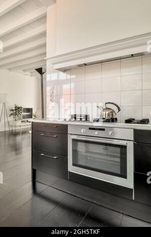 Frammento di interno di moderna cucina open space con forno a muro e pareti piastrellate bianche in spazioso appartamento in stile loft Foto Stock