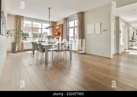 Moderno interno di casa di spaziosa zona pranzo con tavolo e sedie di fronte alla grande finestra in appartamento open space con pareti bianche e pavimento in legno Foto Stock