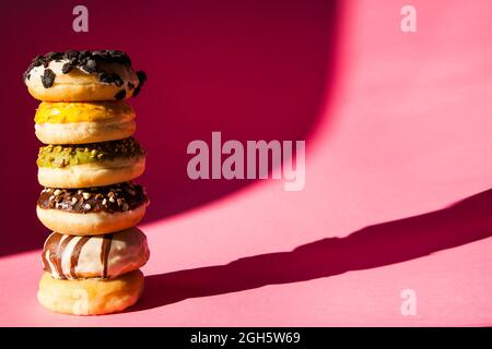 Torre di ciambelle di diversi colori e sapori su sfondo rosa Foto Stock