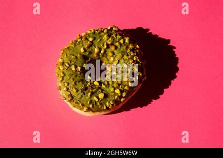 Vista dall'alto di una ciambelle ricoperte di zucchero verde con noci su sfondo rosa Foto Stock