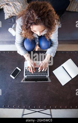 Vista dall'alto della donna d'affari con capelli ricci seduti nel divano e lavorando con il suo laptop Foto Stock