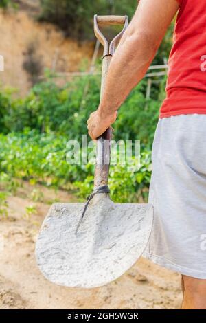 Vista posteriore del coltivatore anonimo maschio con pala in piedi in campo in fattoria in estate Foto Stock