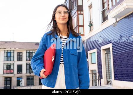 Allegro freelance femminile con netbook in rosso caso in piedi in città strada e guardando avanti Foto Stock