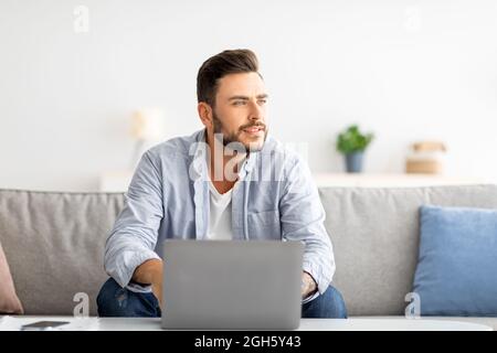 Freelance millennial che lavora su un notebook e guarda da parte, pensando a una strategia aziendale di successo, spazio libero Foto Stock