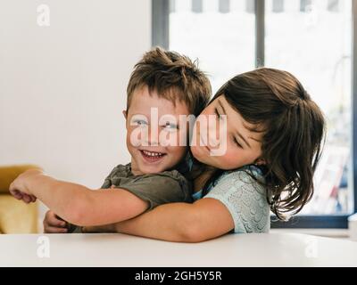 Simpatici gemelli che abbracciano teneramente e si siedono insieme in salotto a casa Foto Stock