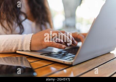 La giovane studentessa latino-americana, dal taglio irriconoscibile, legge le informazioni sullo schermo del computer portatile mentre si prepara per l'esame universitario in un accogliente bar Foto Stock