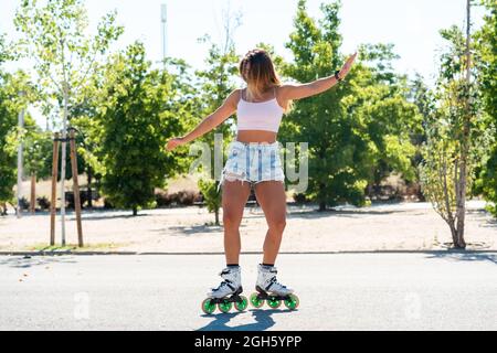 Giovane donna vestita in rollerblade mostrando acrobazie su strada in città in estate Foto Stock