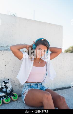 Buona musica femminile giovane ascolto in cuffia durante la giornata di sole in estate in città guardando lontano Foto Stock