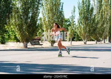 Giovane donna vestita in rollerblade mostrando acrobazie su strada in città in estate Foto Stock