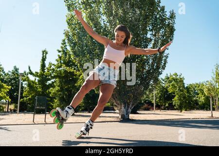 Giovane donna vestita in rollerblade mostrando acrobazie su strada in città in estate Foto Stock