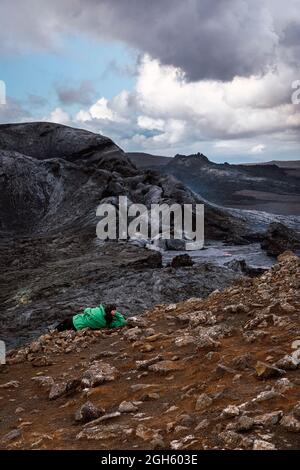 Vista posteriore del viaggiatore irriconoscibile che giace sul monte e contempla Fagradersfjall in Islanda Foto Stock