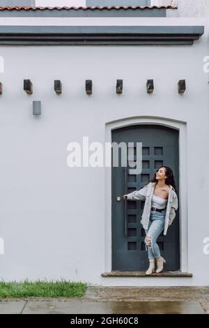 Vista laterale di un giovane conducente maschio seduto in posizione aperta bagagliaio dell'auto e una camicia bianca che si stacca guardando lontano Foto Stock