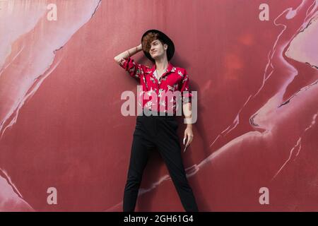 Giovane uomo invano in abbigliamento elegante in piedi sul passaggio piastrellato mentre si guarda la macchina fotografica sulla strada Foto Stock