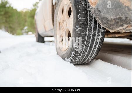 Livello del suolo di pneumatico di ruota di automobile parcheggiato su strada innevata nella foresta di inverno Foto Stock