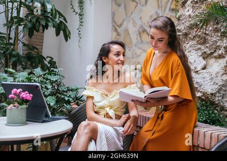 Freelance femminili multirazziali seduti a tavola in un bar tropicale e lavorando al progetto mentre si digita sulla tastiera dock del tablet Foto Stock