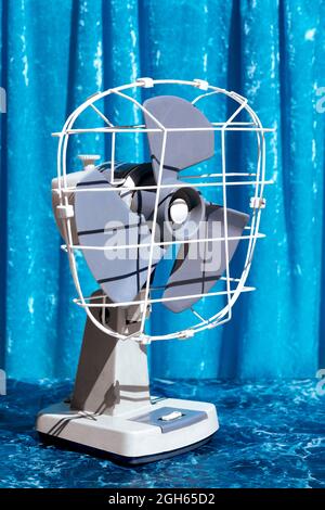 Ventilatore in vecchio stile collocato su un tavolo di marmo in studio su sfondo blu luminoso Foto Stock