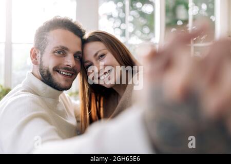 L'uomo allegro barbuto con la donna sincera amata che prende il ritratto di auto mentre osserva la macchina fotografica a casa Foto Stock