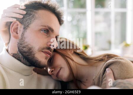 Sorridendo giovane femmina stroking capelli di maschio tatuato amato mentre riposato in casa il giorno di sole Foto Stock