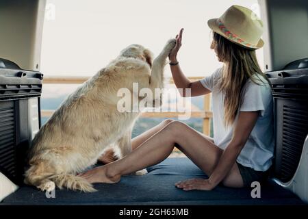 Fedele Golden Retriever cane dando alti cinque a piedi nudi Donna mentre si siede sul letto interno RV durante viaggio in natura Foto Stock