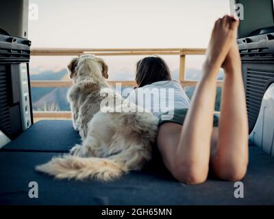 Irriconoscibile femmina turista e obbediente Golden Retriever cane sdraiato sul materasso all'interno camper e ammirando la natura Foto Stock