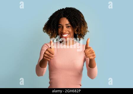 Tutto è grande. Giovane donna nera positiva che mostra le miniature in alto alla fotocamera Foto Stock