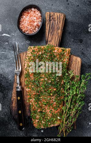 Salmone affumicato con aneto e sale su tavola di legno. Sfondo nero. Vista dall'alto Foto Stock