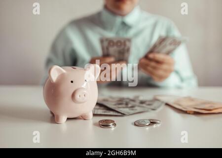 le mani femminili tengono una banca rosa del piggy e mette una moneta là. Il concetto di risparmio di denaro o di risparmio, di investimento Foto Stock