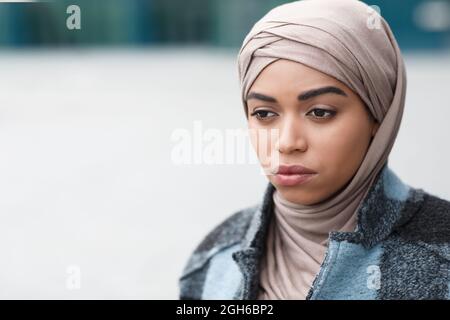 Primo piano ritratto di depressi sconvolto africano americano donna, signora premurosa in hijab e cappotto in città all'aperto Foto Stock