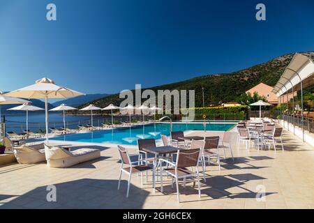 Piscina di lusso con sedie a sdraio, tavoli e ombrelloni vuoti presso il resort con splendida vista sul mare. Isola greca. Foto Stock