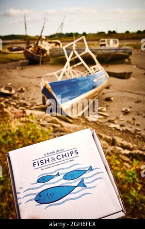 Una scatola di cartone contenente pesce e patatine di fronte ai pescherecci da traino abbandonati nel bacino ittico Wyre di Fleetwood Foto Stock