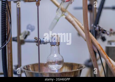 Matraccio a fondo tondo con liquido trasparente per sintesi chimica avanzata in laboratorio chimico con impianto elettrico Foto Stock