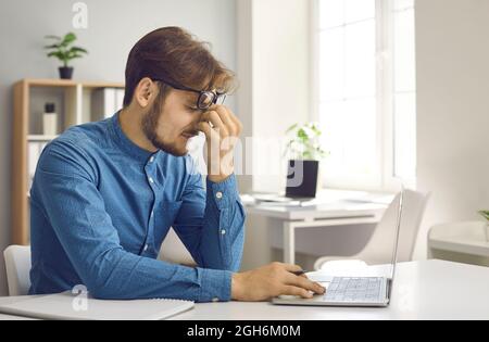 Il lavoratore d'ufficio stanco stressato ha la tensione dell'occhio dal lavoro costante sul calcolatore del laptop Foto Stock
