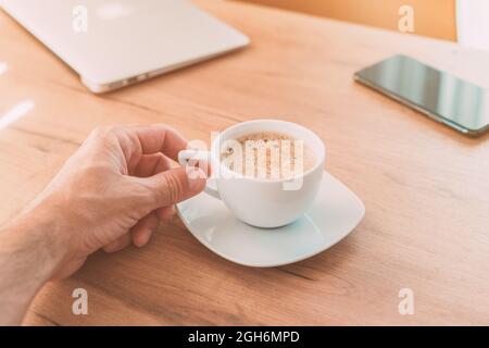 Freelancer bere caffè in ufficio prima di arrivare al lavoro, tenere la tazza a mano, fuoco selettivo Foto Stock