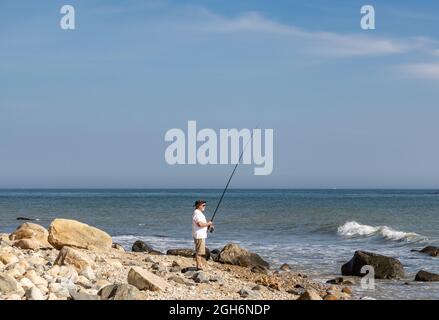 Un uomo che pesca con la canna e bobina fuori Montauk Point, NY Foto Stock