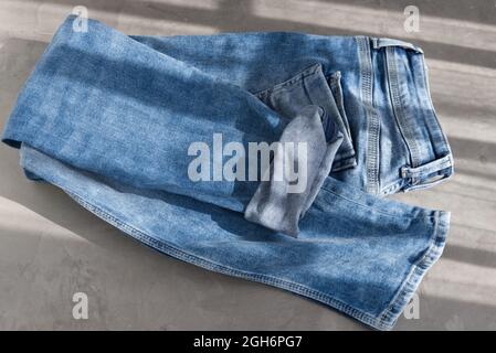 jeans piegati in blu su sfondo grigio. Luce solare Foto Stock