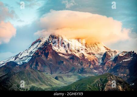 Vista panoramica ravvicinata della montagna di Kazbek coperta da una nuvola soleggiata a Stepantsminda Georgia durante l'alba Foto Stock