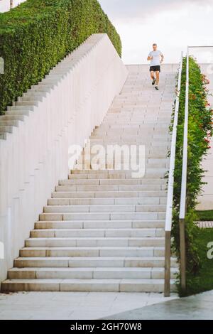 Il giovane atleta fa la corsa mattutina. Il maschio corre giù le scale facendo esercizi cardio. Foto Stock