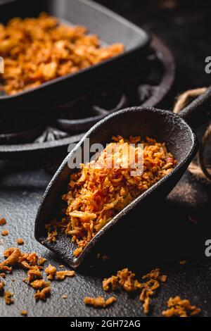 Cipolle fritte fatte in casa in una tazza da cucina in ferro con padella nera su sfondo nero Foto Stock