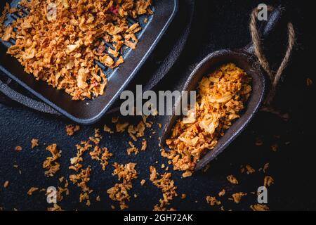 Cipolle fritte fatte in casa in una tazza da cucina in ferro con padella nera su sfondo nero Foto Stock