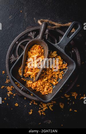 Cipolle fritte fatte in casa in una tazza da cucina in ferro con padella nera su sfondo nero Foto Stock