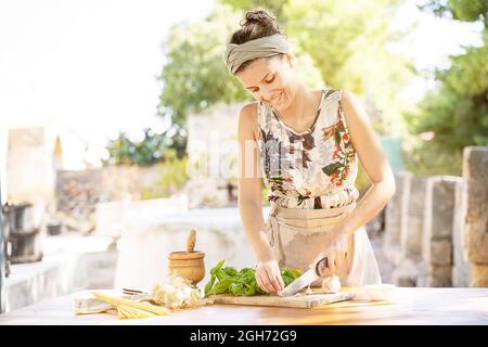 Donna tritare mazzo di basilico su un tagliere di legno all'aperto Foto Stock