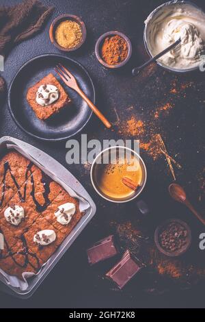 Brownie fatte in casa con una tazza di caffè e ingredienti da forno su sfondo marrone Foto Stock