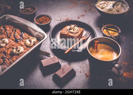 Brownie fatte in casa con una tazza di caffè e ingredienti da forno su sfondo marrone Foto Stock