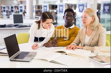 Tutor femminile che aiuta gli studenti a prepararsi per l'esame in biblioteca Foto Stock