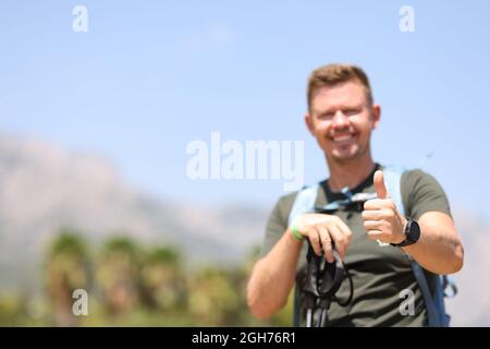Il turista maschio tiene il pollice in su sulla cima della montagna Foto Stock