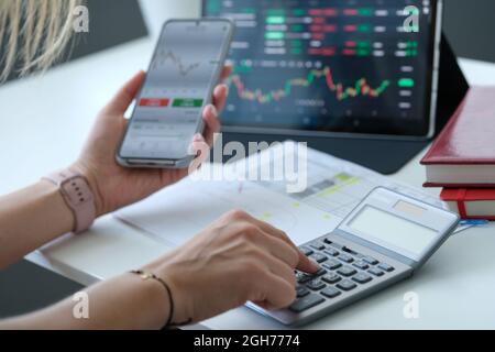 Donna che guarda il grafico sullo schermo del telefono cellulare e conta sul primo piano della calcolatrice Foto Stock