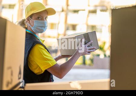 Protezione della salute, sicurezza e pandemia concetto di consegna donna in faccia maschera medica di protezione che tiene la scatola del pacco. Foto Stock