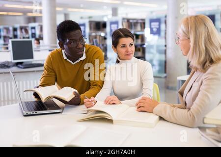 Tutor femminile che aiuta gli studenti a prepararsi per l'esame in biblioteca Foto Stock