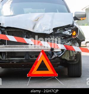 Segnale rosso triangolo di arresto di emergenza e nastro di avvertimento rosso per la polizia prima auto distrutta in auto incidente stradale incidente sulla strada della città. Ha rotto la macchina dentro Foto Stock