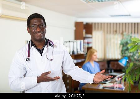 Sorridente medico afroamericano che dà il benvenuto all'ufficio medico Foto Stock